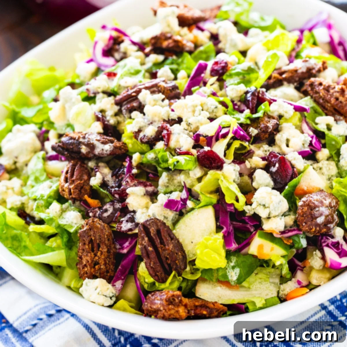 A vibrant Blue Cheese Chopped Salad topped generously with Craisins and Candied Pecans, served in a large white bowl, ready to be enjoyed.