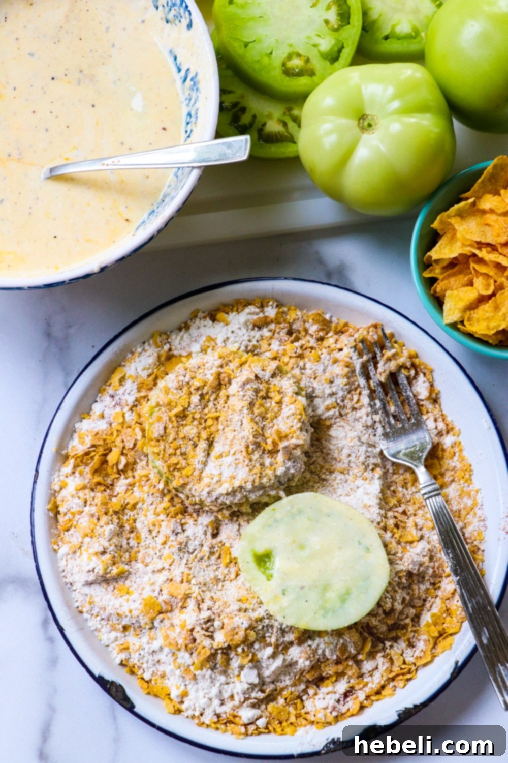 Green tomato slices being coated in a cornflake crumb mixture.