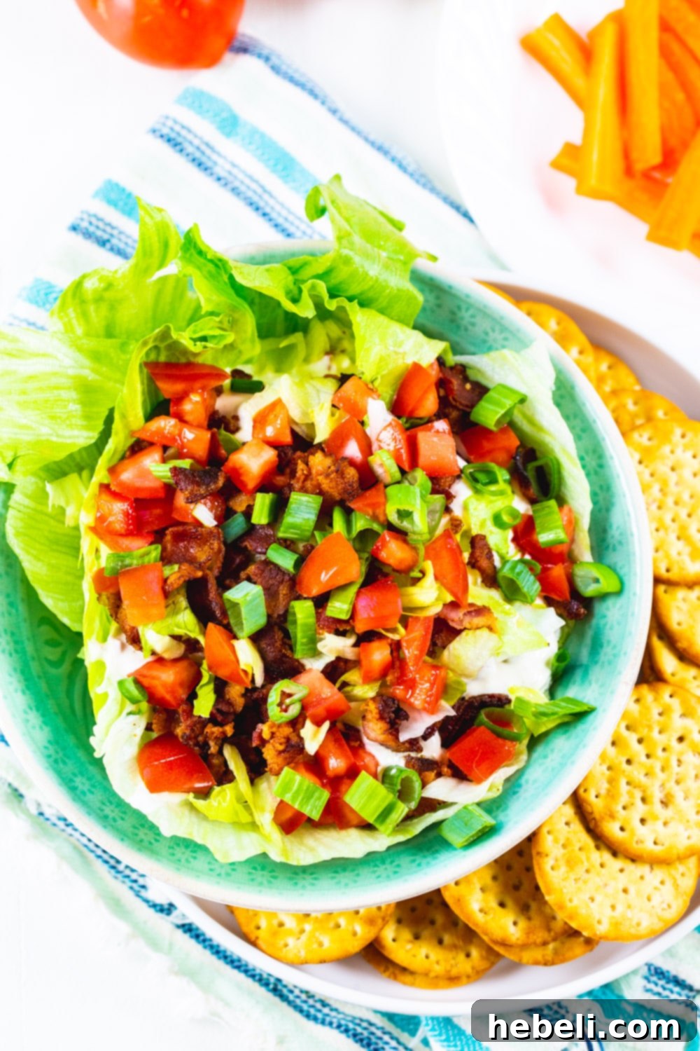Creamy BLT Dip 3 Overhead shot of creamy BLT Dip in a white bowl, garnished with fresh toppings, sitting on a wooden plate with an array of crackers.