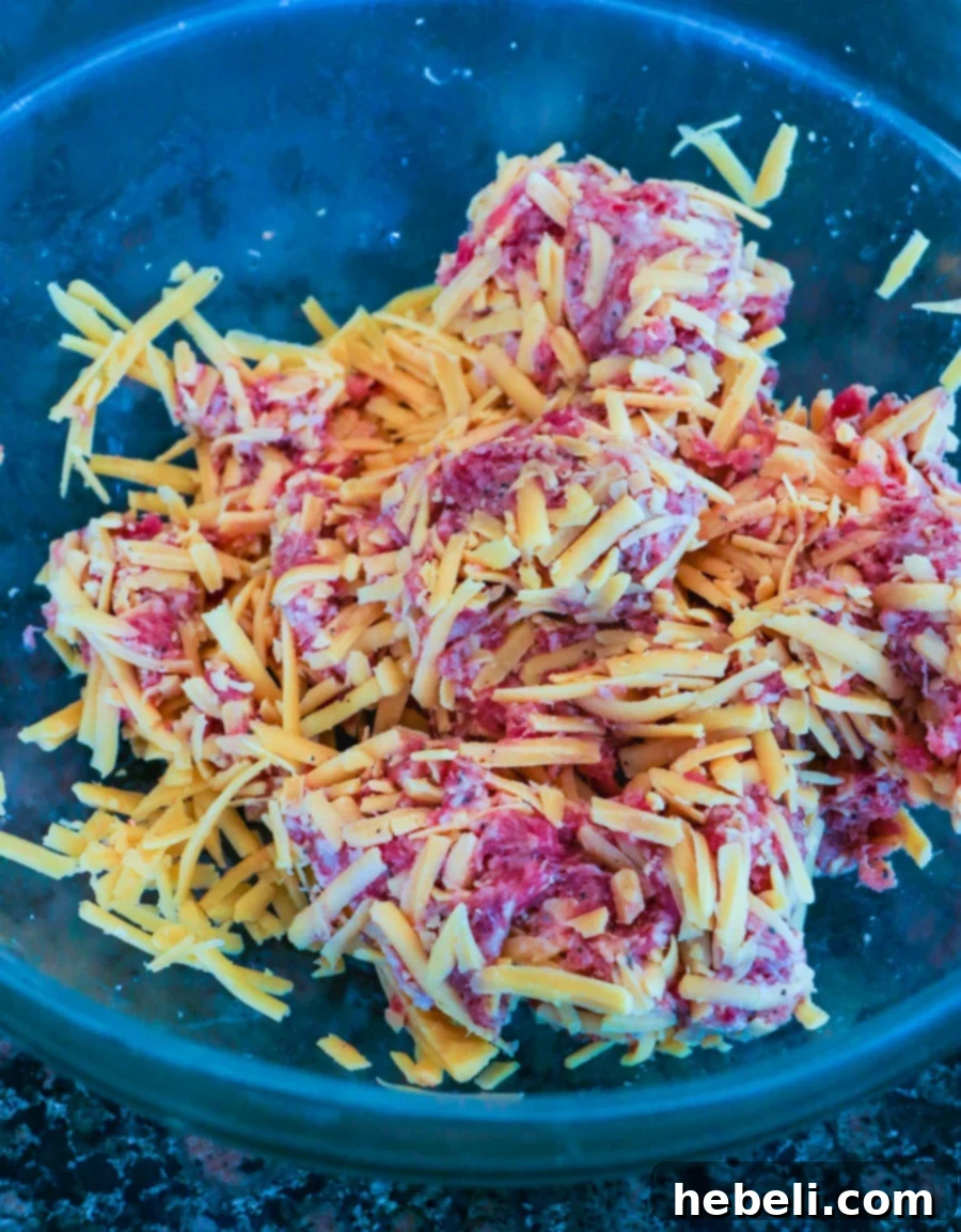A large bowl showing ground breakfast sausage and shredded cheddar cheese mixed together, ready for the next step.