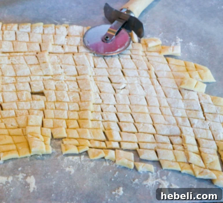 Close-up of crescent dough cut into small, uniform squares using a pizza cutter, prepared for mixing.