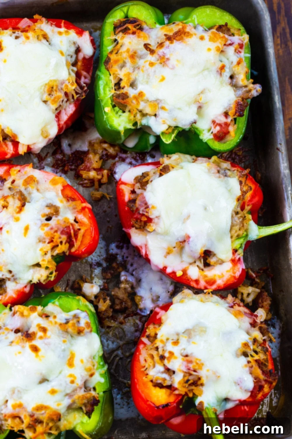 Six cooked Italian Sausage Stuffed Peppers on a baking sheet, topped with melted cheese.