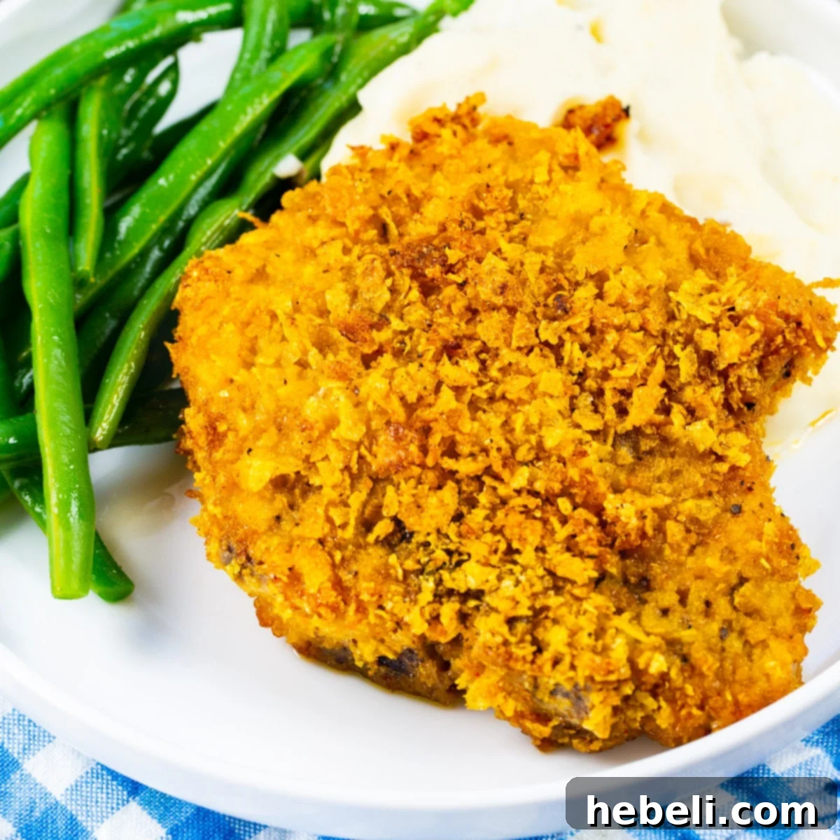 Golden-brown Cornflake Crusted Baked Pork Chops on a plate, served with fluffy mashed potatoes and vibrant green beans, ready for a delicious meal.
