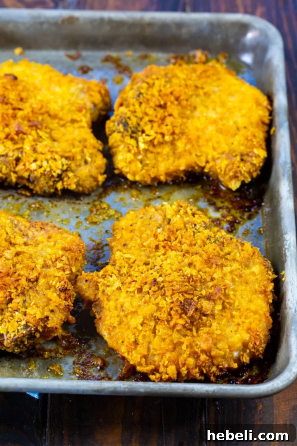 Cornflake Crusted Baked Pork Chops arranged neatly on a greased baking sheet, showcasing their crisp coating before baking.