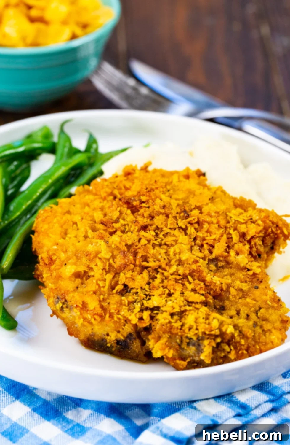 A close-up of a perfectly cooked Cornflake Crusted Baked Pork Chop, served with a generous scoop of mashed potatoes and a side of green beans, creating a wholesome meal.
