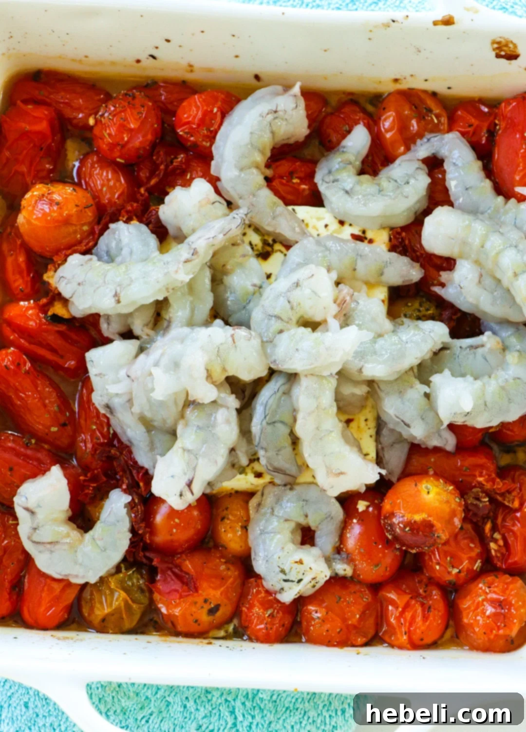 Fresh, uncooked shrimp are carefully added to the baking dish, nestled among the roasted tomatoes and partially melted feta cheese, ready for the final baking phase.