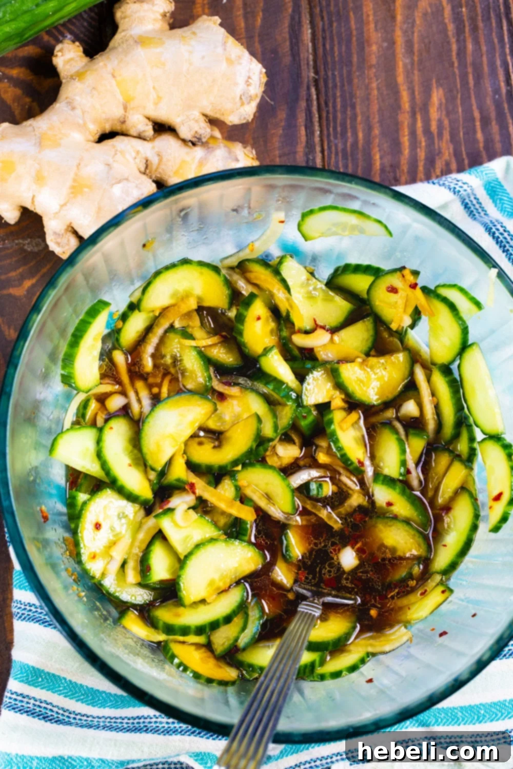 A clear glass bowl showcasing fresh cucumber slices, sweet onion, and all the individual ingredients for the dressing, poised for mixing.