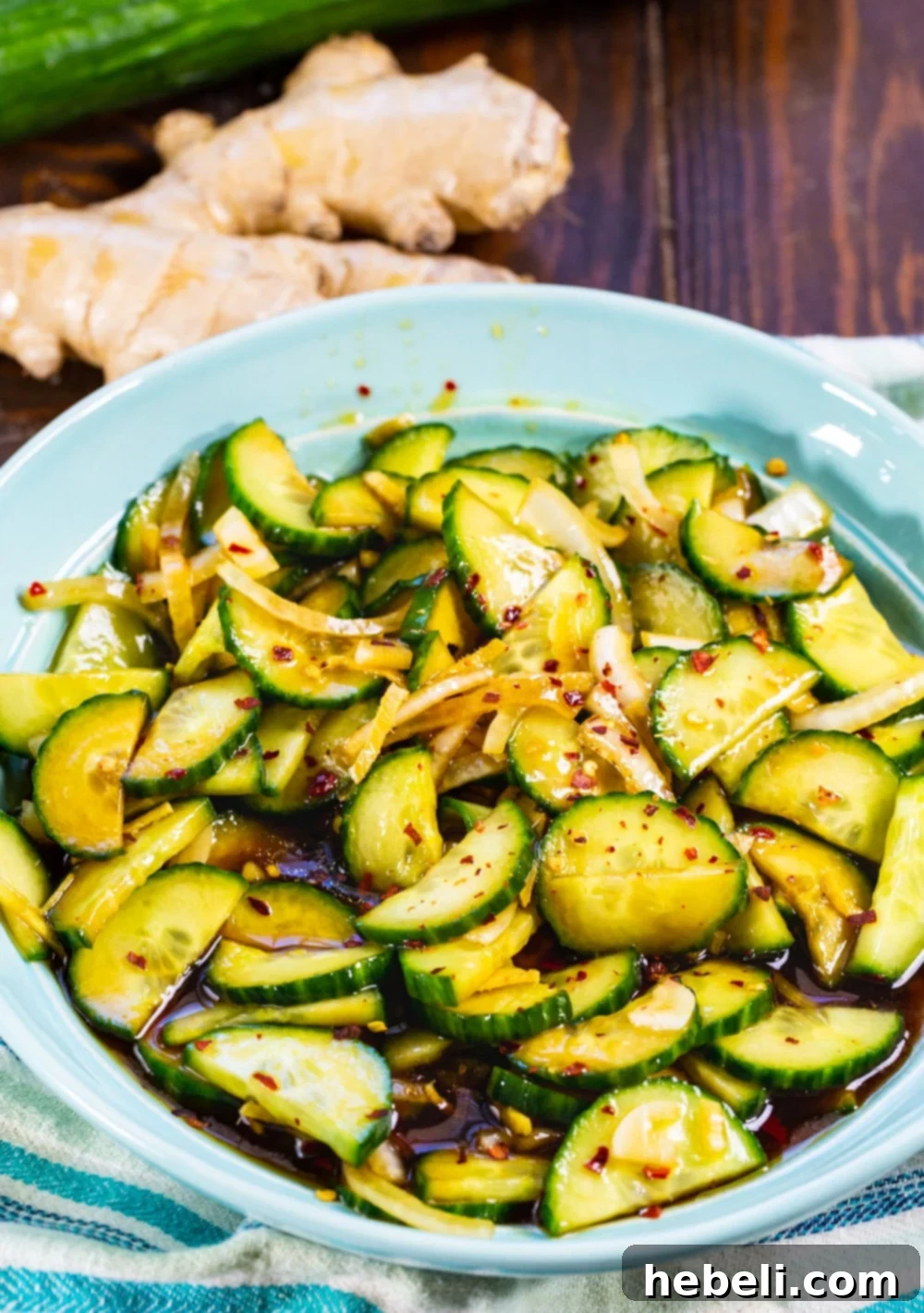 A close-up shot of Ginger Sesame Cucumbers in a blue ceramic bowl, highlighting the intricate slices and appetizing dressing.