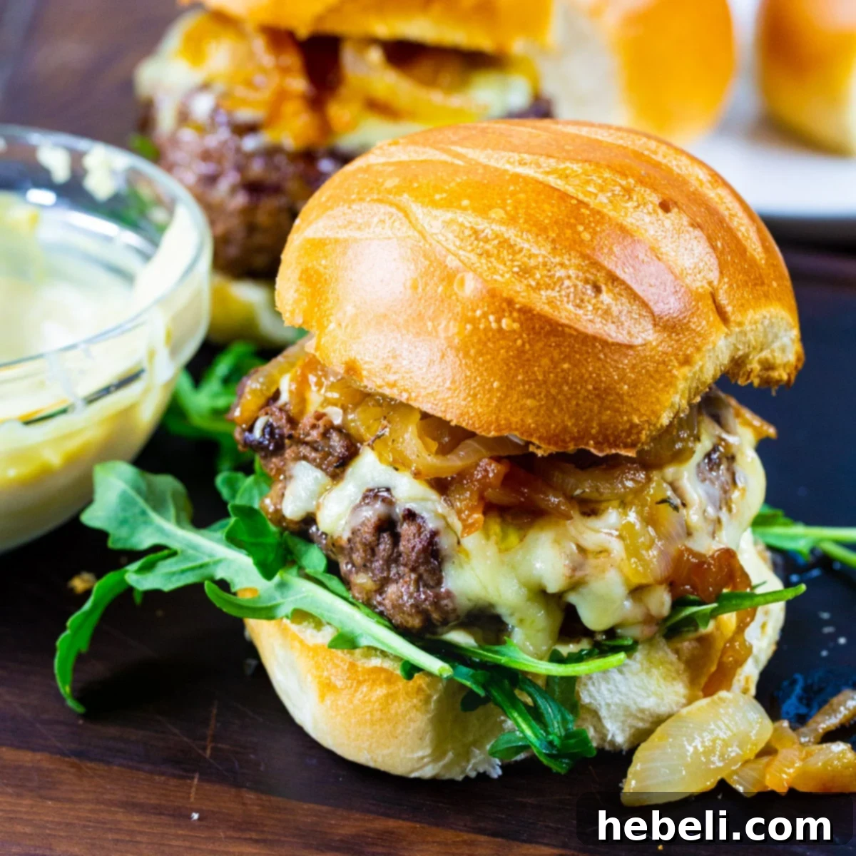 French Onion Burgers on brioche buns with arugula, showcasing the melted cheese and caramelized onions.