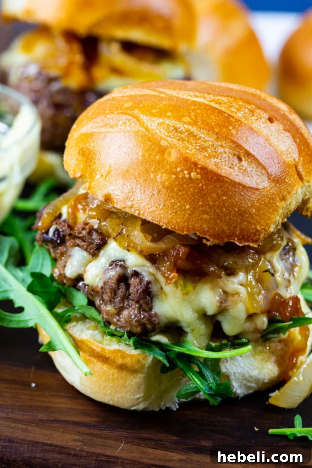 Close-up of a French Onion Burger, revealing the melted Gruyere, caramelized onions, and garlic Dijonnaise on a toasted brioche bun.
