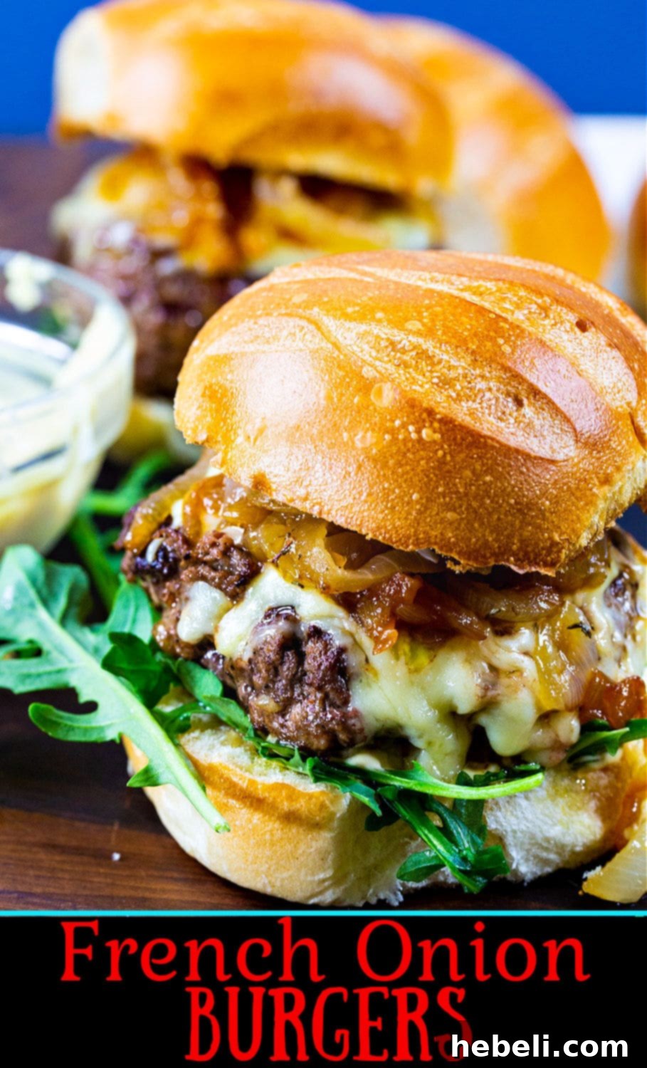 French Onion Burgers with gruyere cheese and caramelized onions on a rustic wooden board.