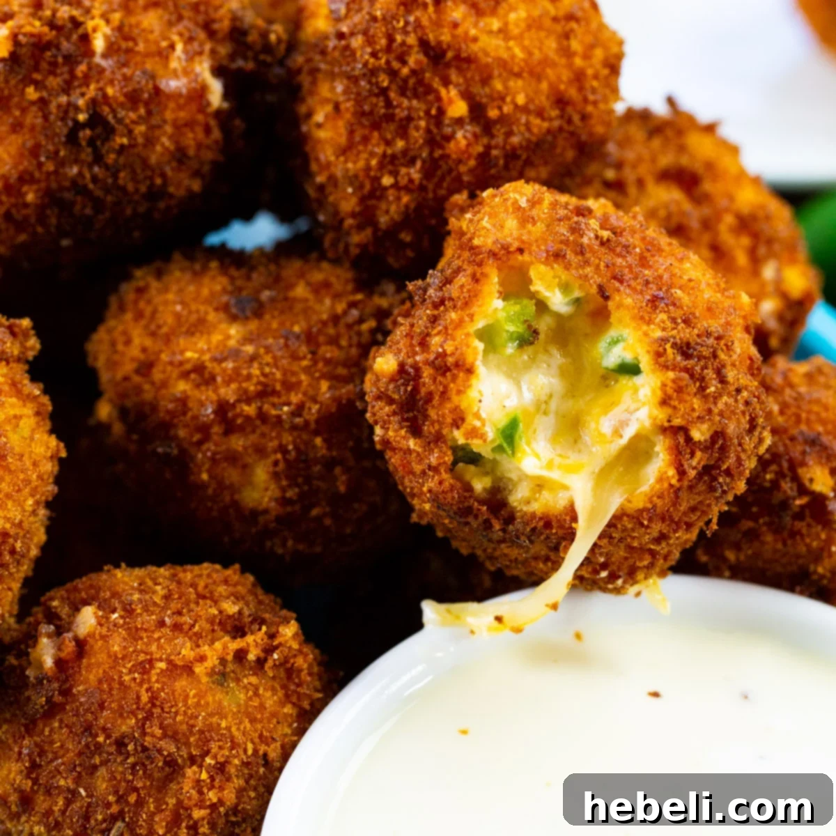Crispy Jalapeno Poppers 2 Fried Jalapeno Popper Bites with a bite taken out, revealing the creamy, cheesy interior.