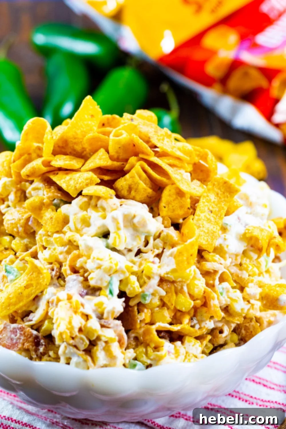 Creamy Jalapeno Frito Corn Salad 4 Jalapeno Popper Corn Frito Salad in a white serving bowl with fresh jalapenos and ingredients in the background.