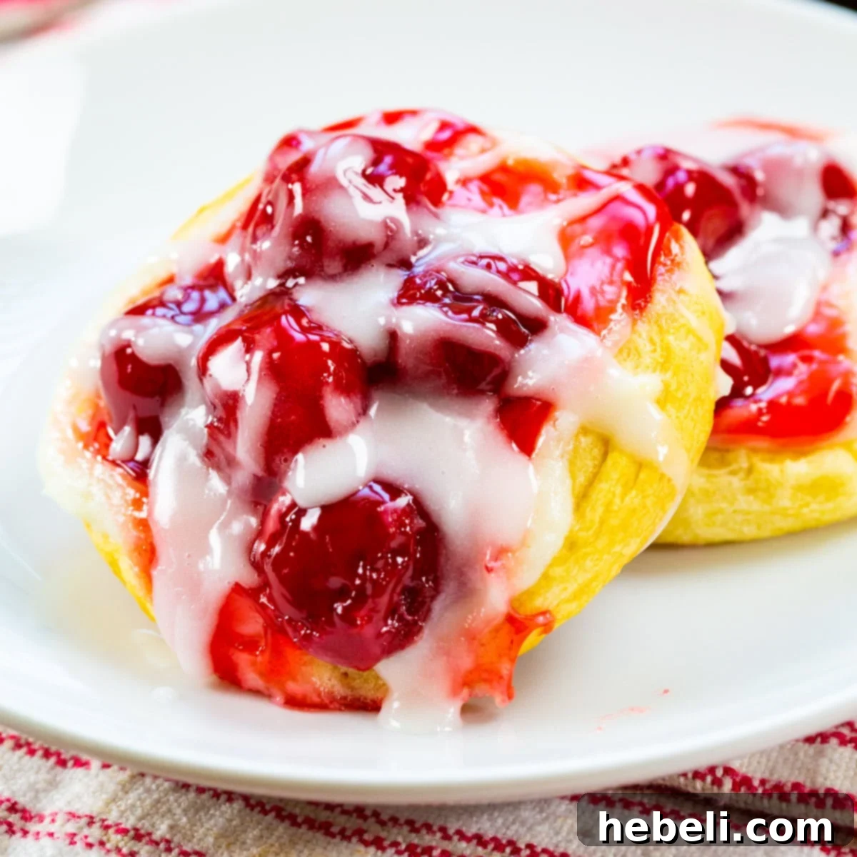 Flaky Cherry Danishes Made Simple 2 Two golden-brown cherry danishes with white glaze on a plate, ready to be enjoyed.