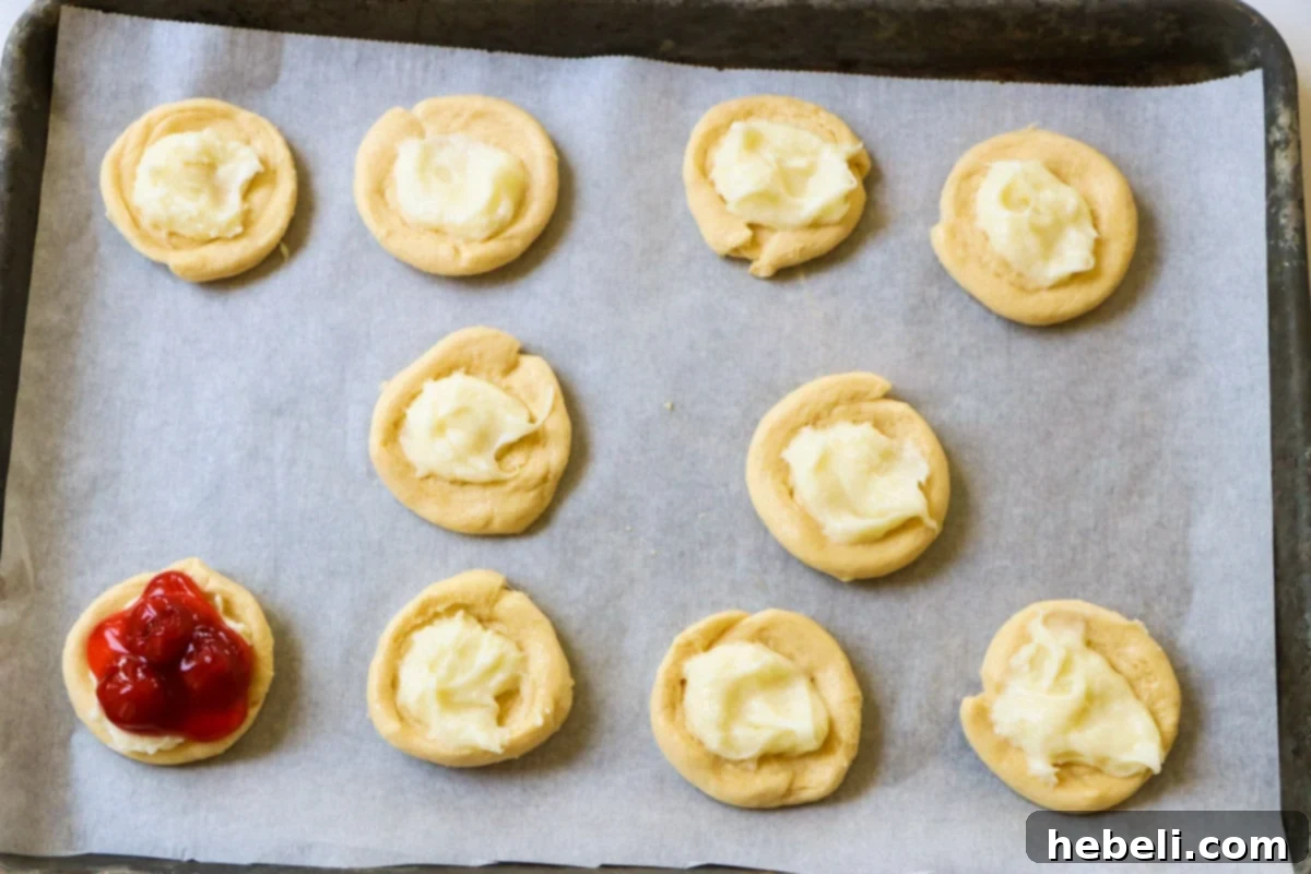Flaky Cherry Danishes Made Simple 3 Unbaked cherry danishes arranged neatly on a baking sheet lined with parchment paper, awaiting oven time.