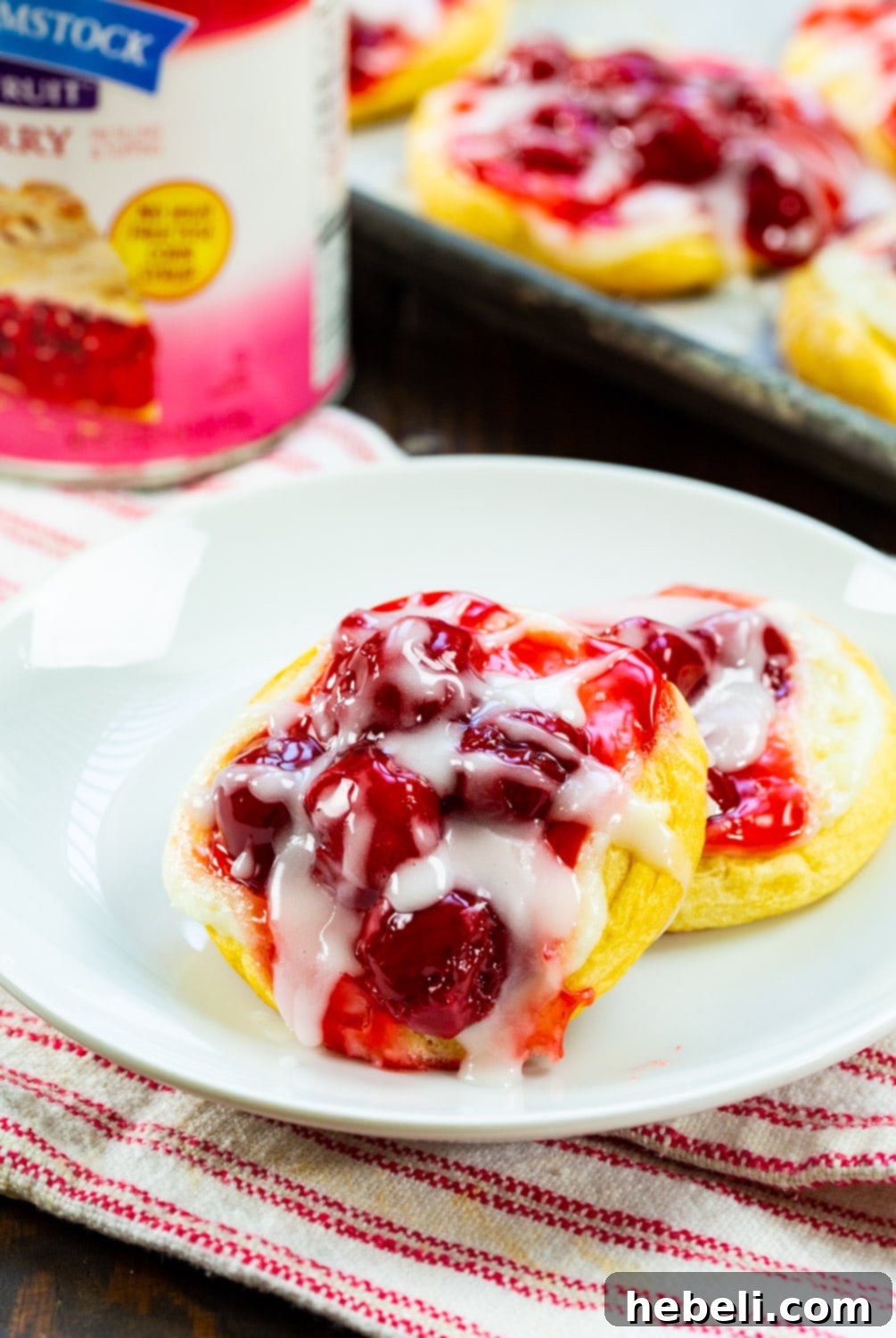 Flaky Cherry Danishes Made Simple 5 Two glazed cherry danishes on a white plate, showcasing their inviting texture and rich filling.