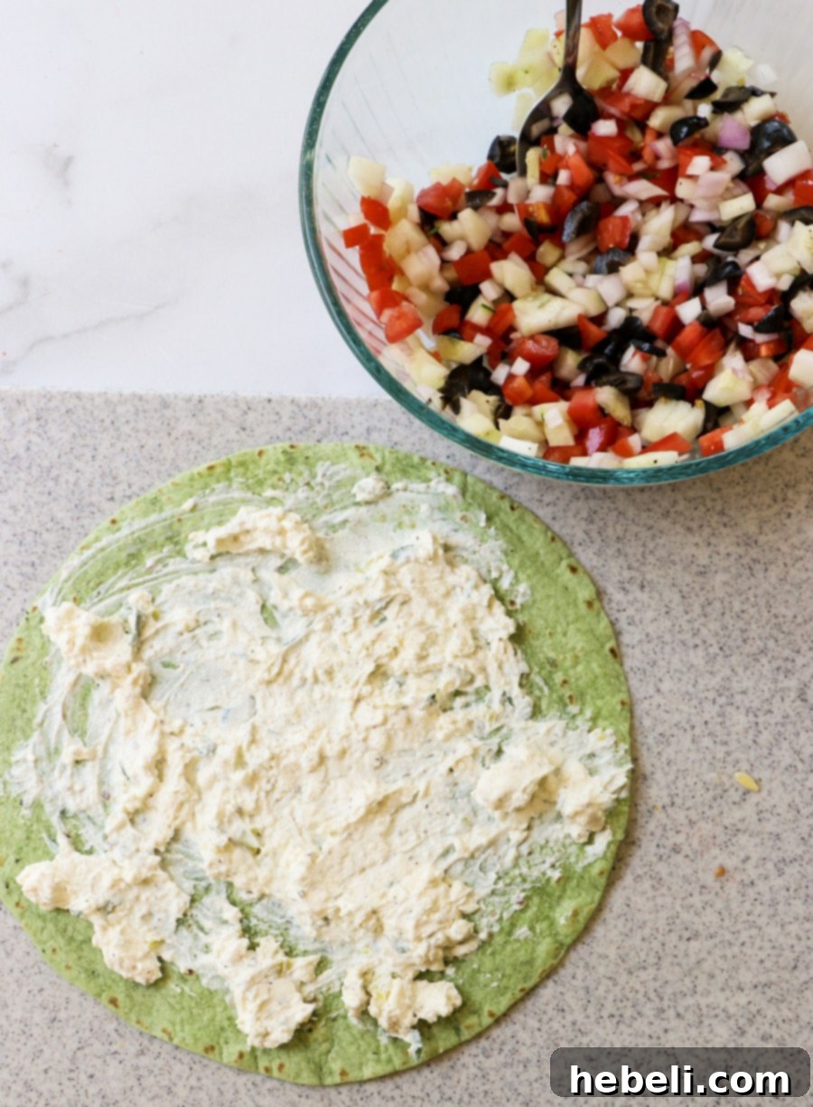 Mediterranean Swirl Appetizers 4 A step-by-step image showing the creamy cream cheese mixture being smoothly spread onto a spinach tortilla, ready for the delicious fillings.