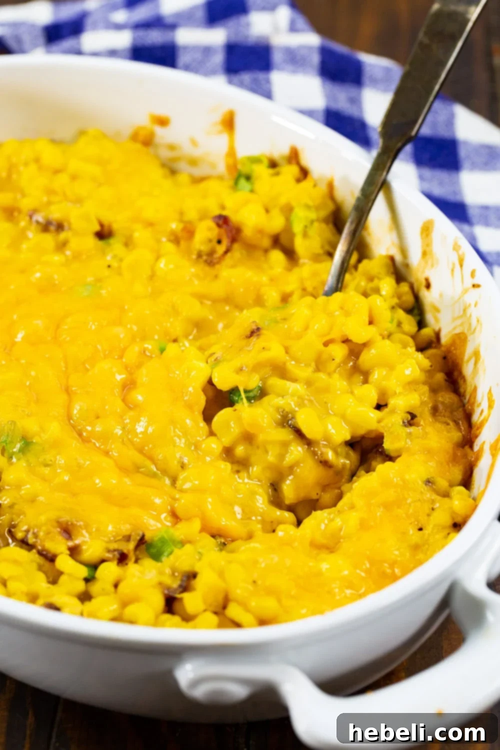 A spoon scooping a generous portion of warm Cheesy Corn Casserole, showing its creamy texture and bacon bits.