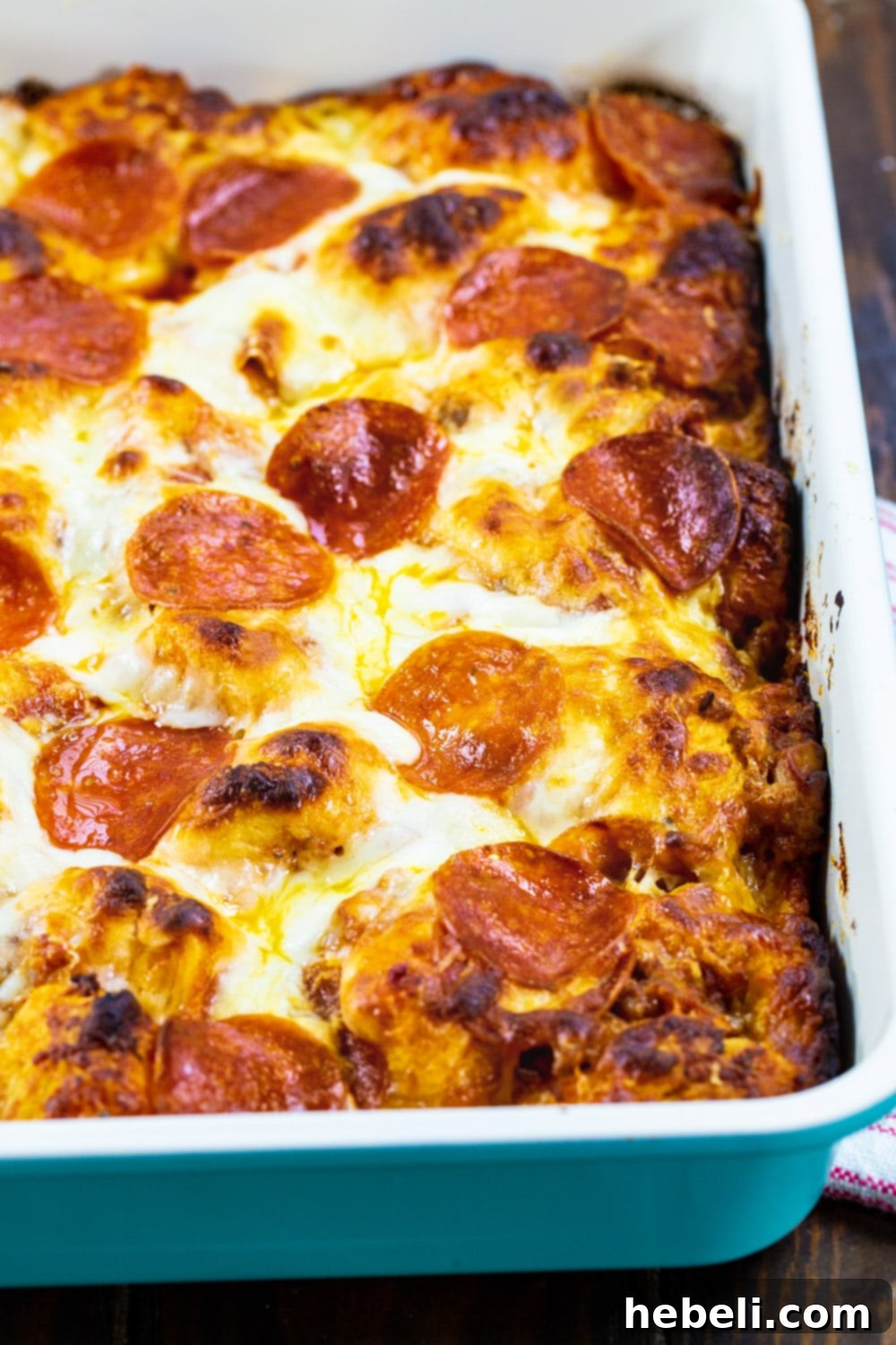 The unbaked Meat Lovers Bubble Up Pizza casserole in a 9x13-inch baking pan, showing the biscuit pieces, sausage, pepperoni, and cheese ready for baking.