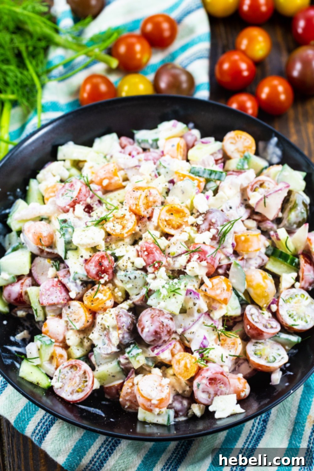 Close-up of Creamy Tomato and Cucumber Chopped Salad in a black bowl, surrounded by fresh, colorful tomatoes.