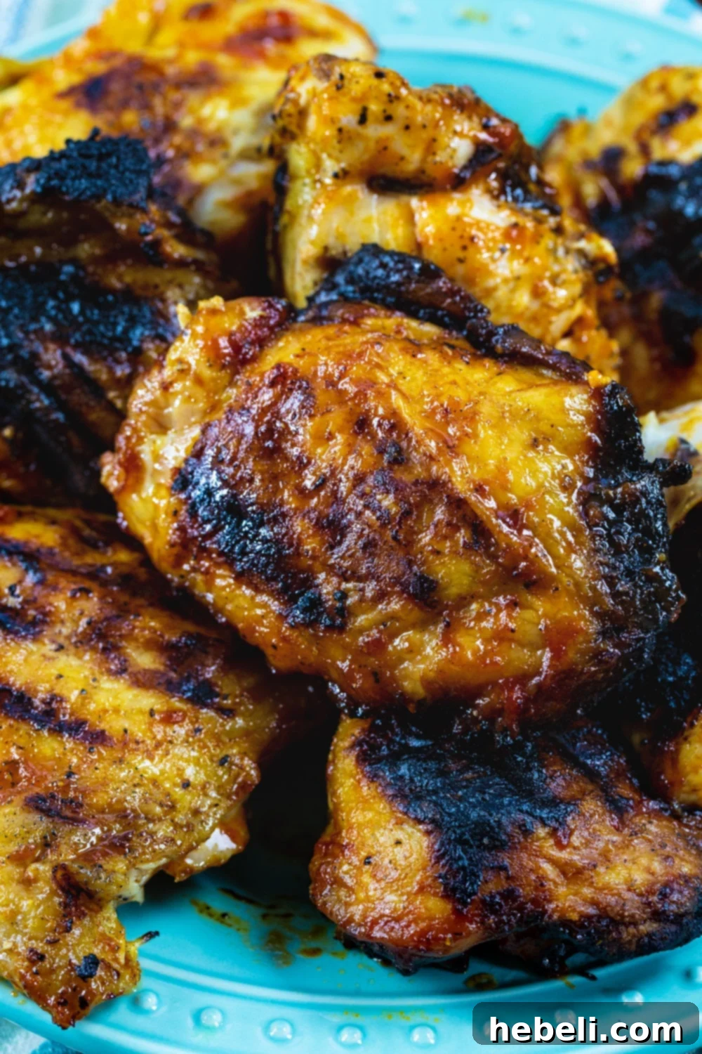 Grilled chicken pieces piled high on a serving plate, showcasing their crispy skin and golden-brown hue.