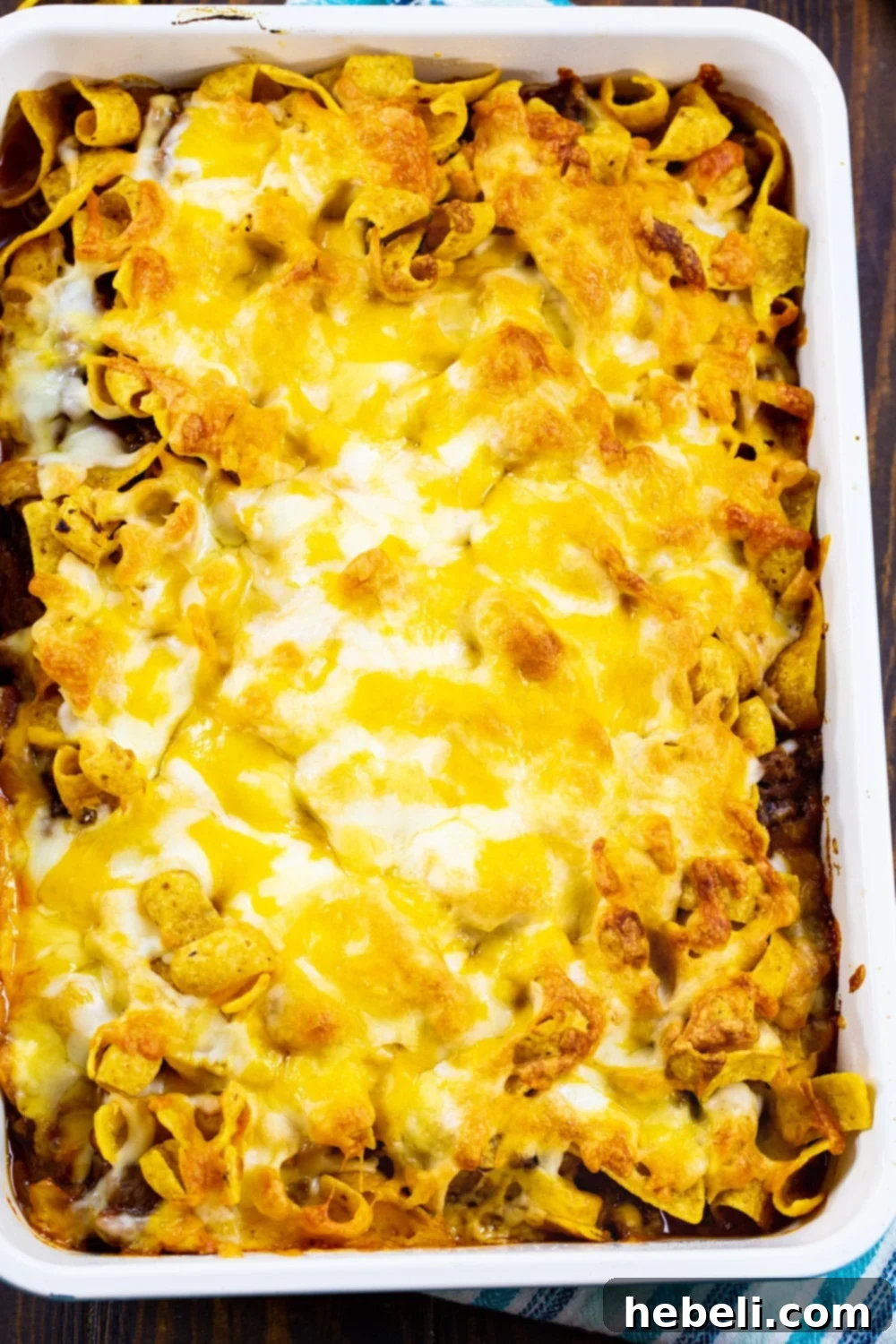 Overhead view of a 9x13-inch pan filled with Sloppy Joe Frito Casserole before baking, showing the Frito chips and shredded cheese topping.
