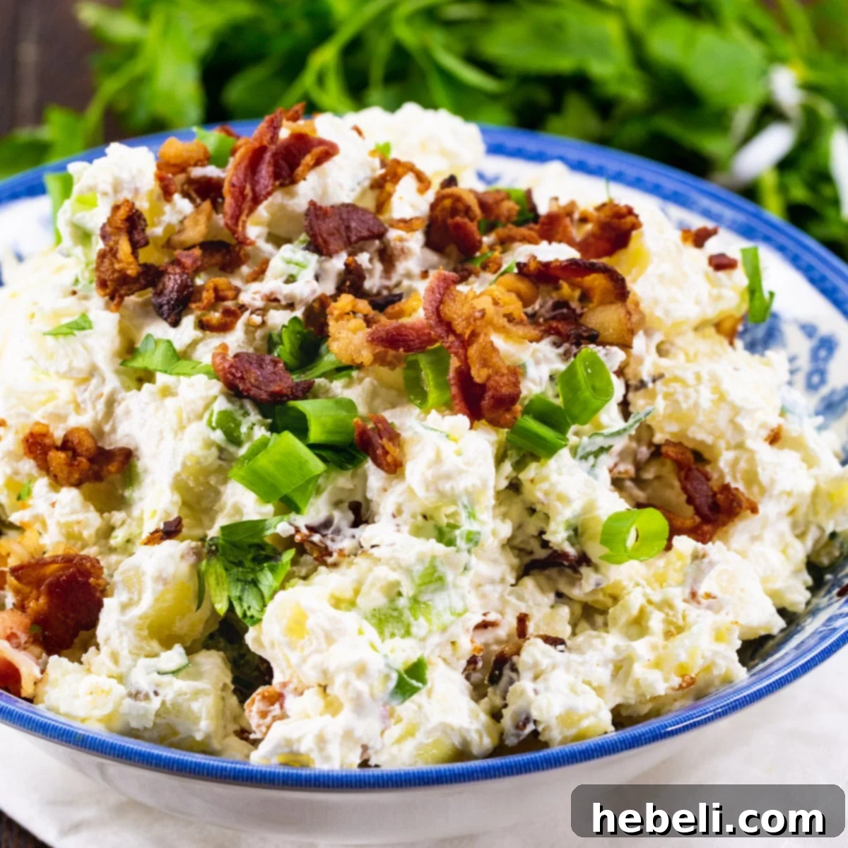 Creamy Bacon Potato Salad 2 A vibrant blue and white bowl filled with creamy Sour Cream and Bacon Potato Salad, garnished with fresh green onions and crispy bacon bits.