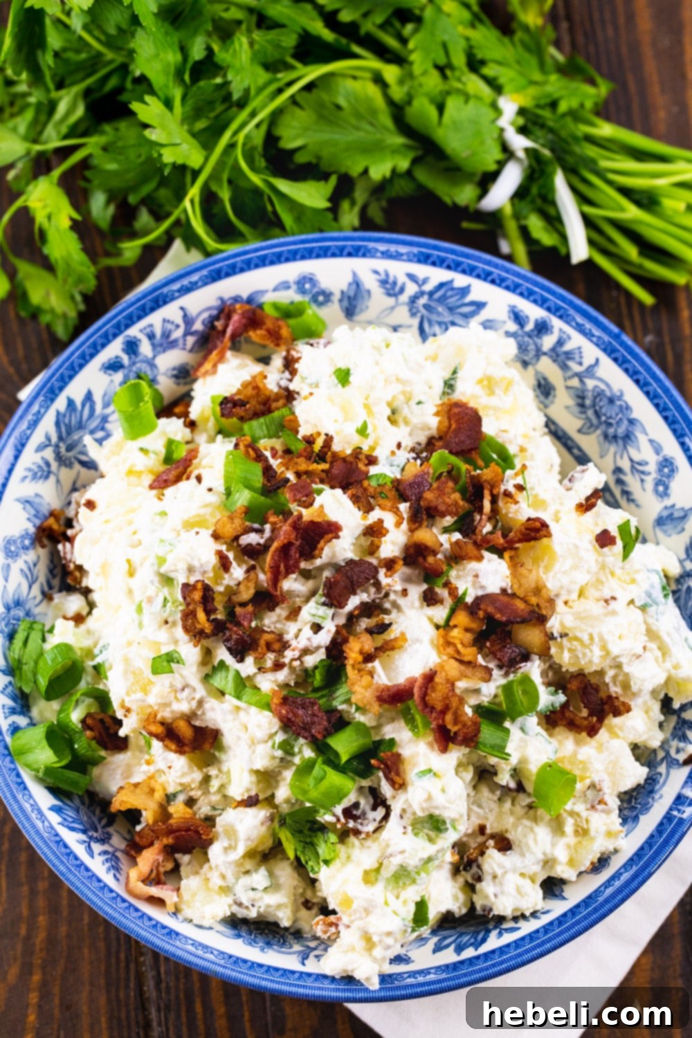 Creamy Bacon Potato Salad 3 Overhead shot of a bowl of Sour Cream and Bacon Potato Salad, beautifully garnished with fresh parsley sprigs and a side of chopped herbs.