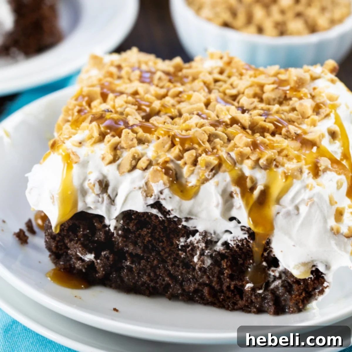 A delectable slice of Toffee Poke Cake on a plate, showcasing layers of chocolate cake, caramel, and a fluffy whipped topping adorned with toffee.