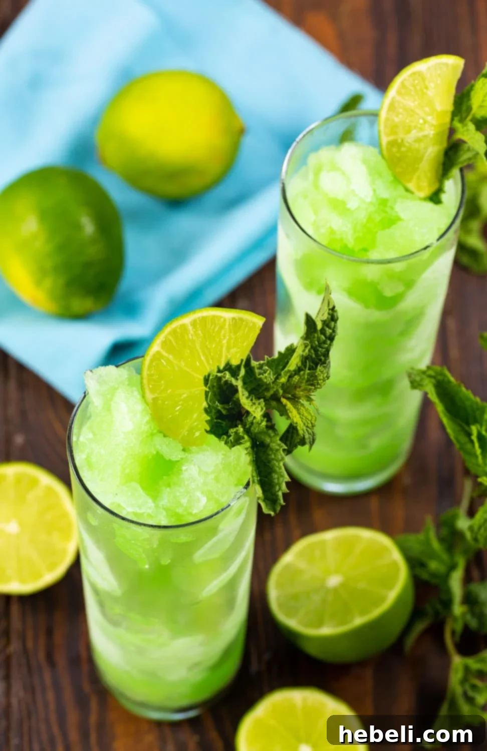 Two glasses filled with Mojitos with lime halves surrounding them.
