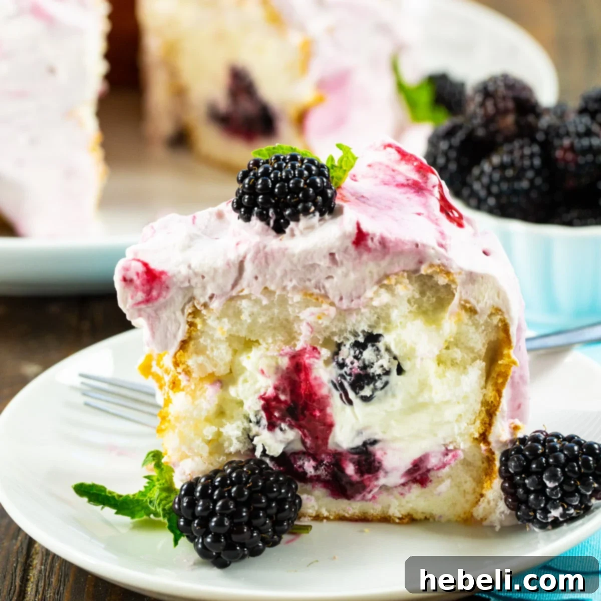 A beautiful slice of Blackberries and Cream Angel Food Cake presented on a white plate, showcasing the creamy filling and blackberry swirl.