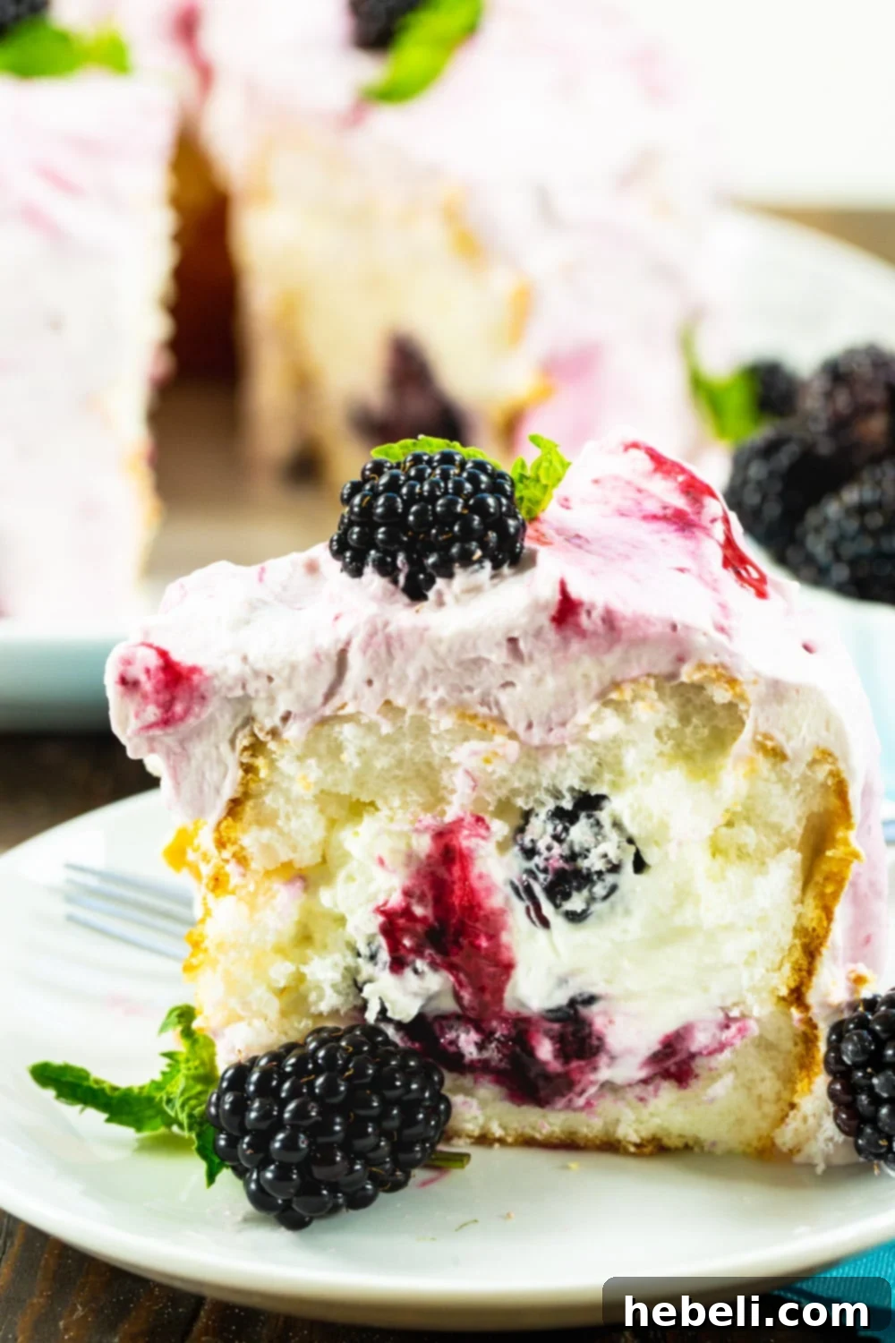 A close-up shot of a slice of Blackberries and Cream Angel Food Cake garnished with fresh blackberries.