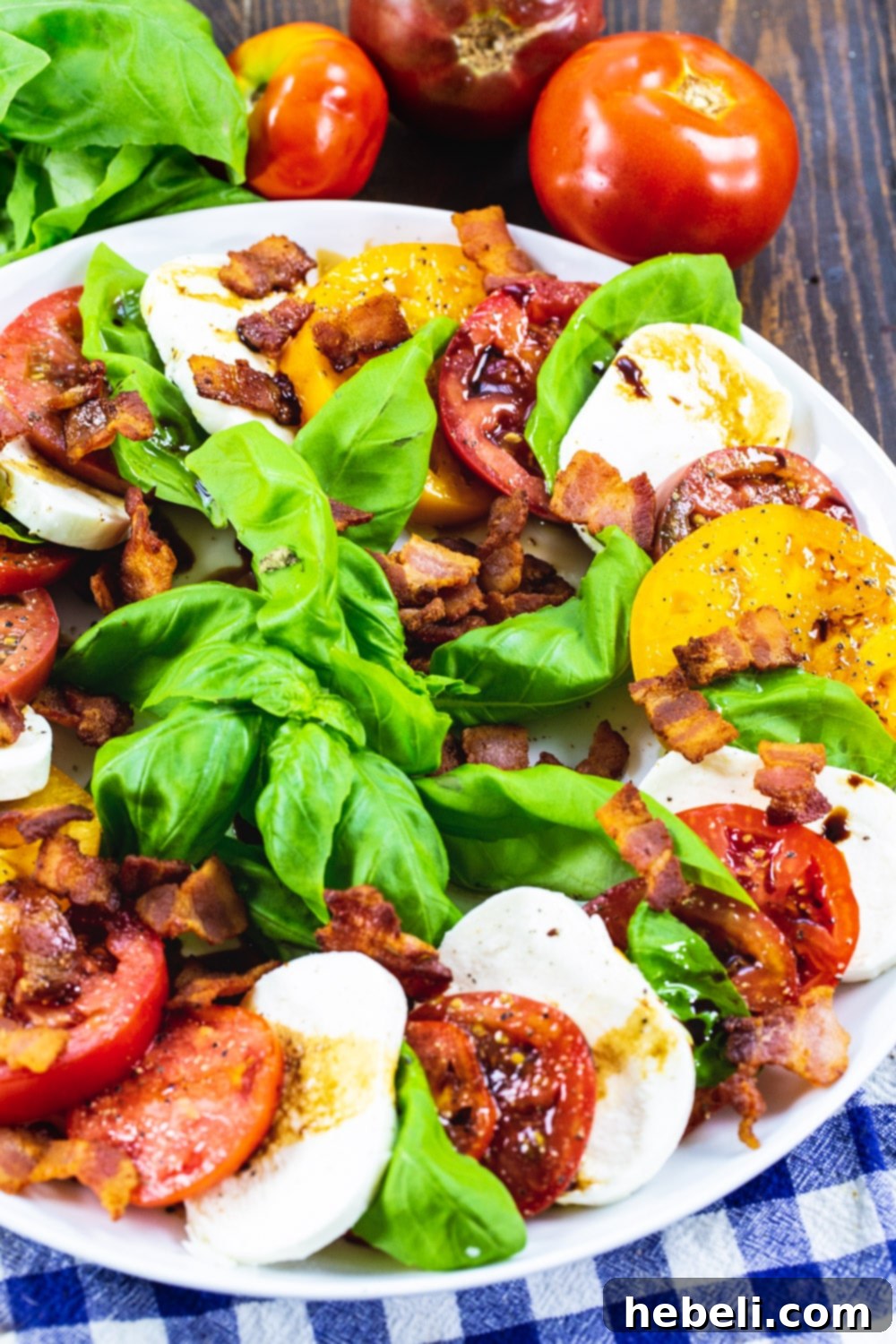 A close-up of Bacon Caprese Salad served on a white plate, highlighting the crispy bacon bits, fresh basil, and creamy mozzarella against ripe tomato slices.