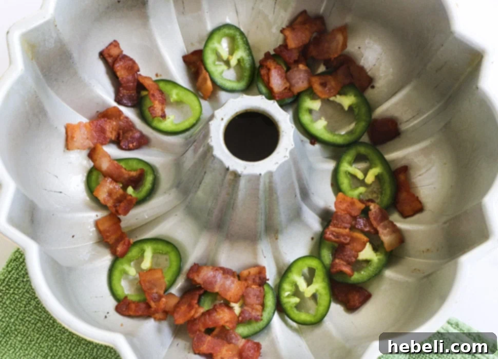 Gooey Jalapeno Cheese Bombs 3 Bacon pieces and jalapeno slices in bottom of bundt pan, ready for biscuit layers.