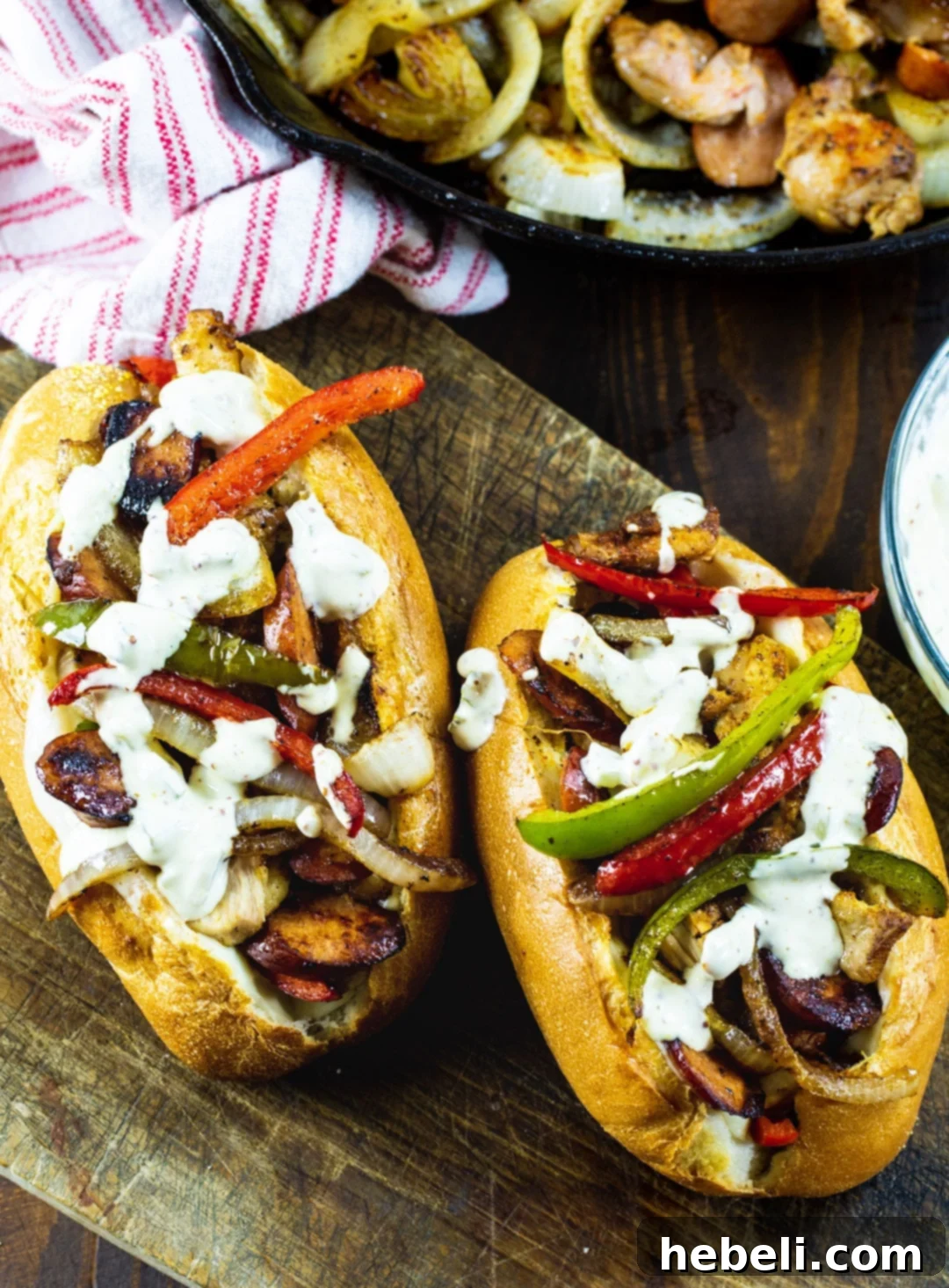 Two perfectly assembled Cajun Chicken and Andouille Subs next to a skillet filled with the savory chicken and sausage mixture.