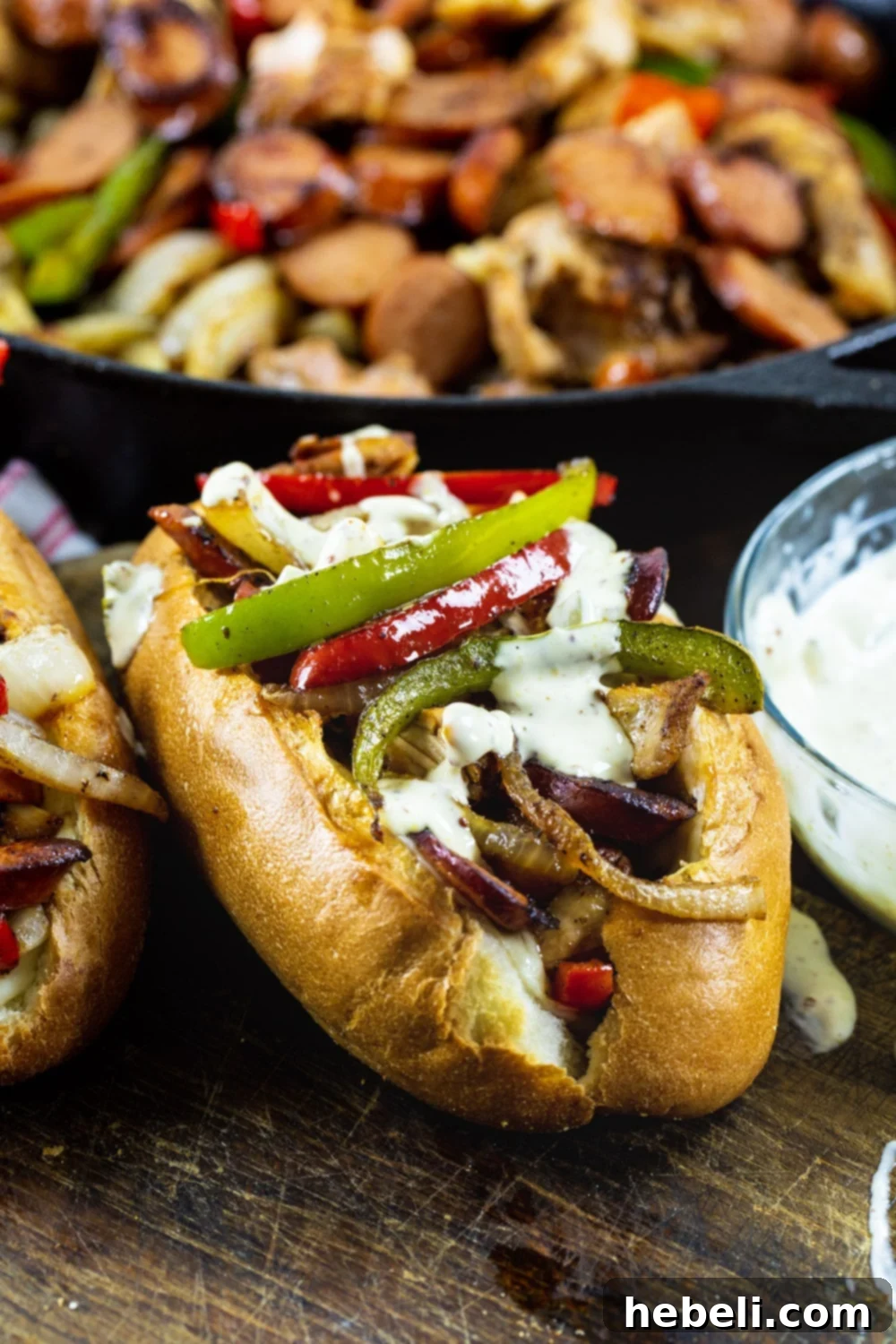 Three Cajun Chicken and Andouille Subs artfully arranged, with a cast iron skillet holding the delicious filling visible in the soft background.