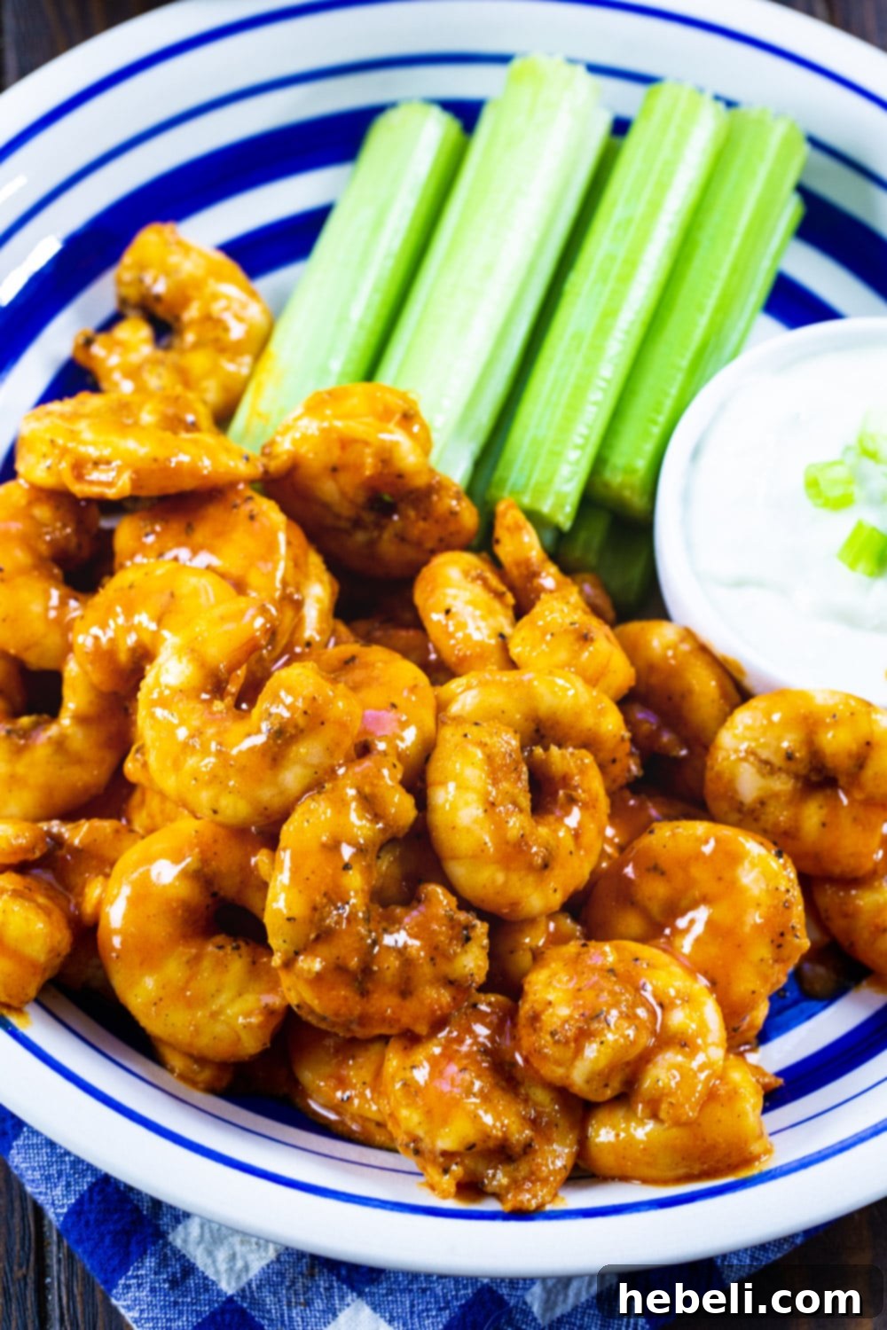 Close-up of shrimp coated in buffalo sauce, arranged neatly on a blue and white patterned plate.