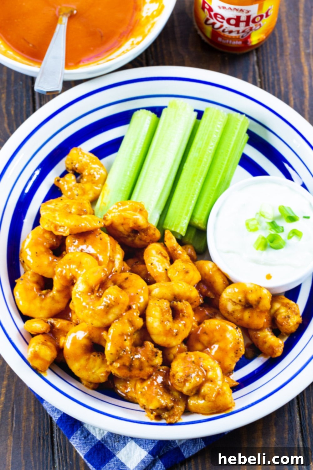 A plate of Broiled Buffalo Shrimp garnished with fresh parsley, served with crunchy celery and a side of blue cheese dressing.