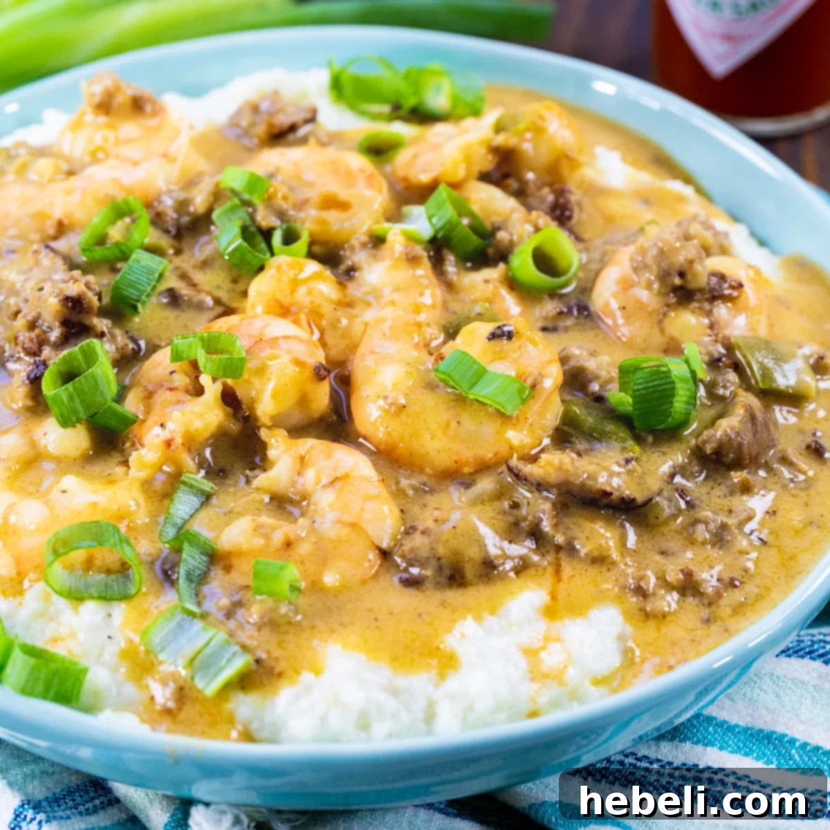 A vibrant blue bowl filled with creamy grits, topped with rich sausage gravy and succulent shrimp, garnished with fresh green onions. A true Southern comfort food delight.