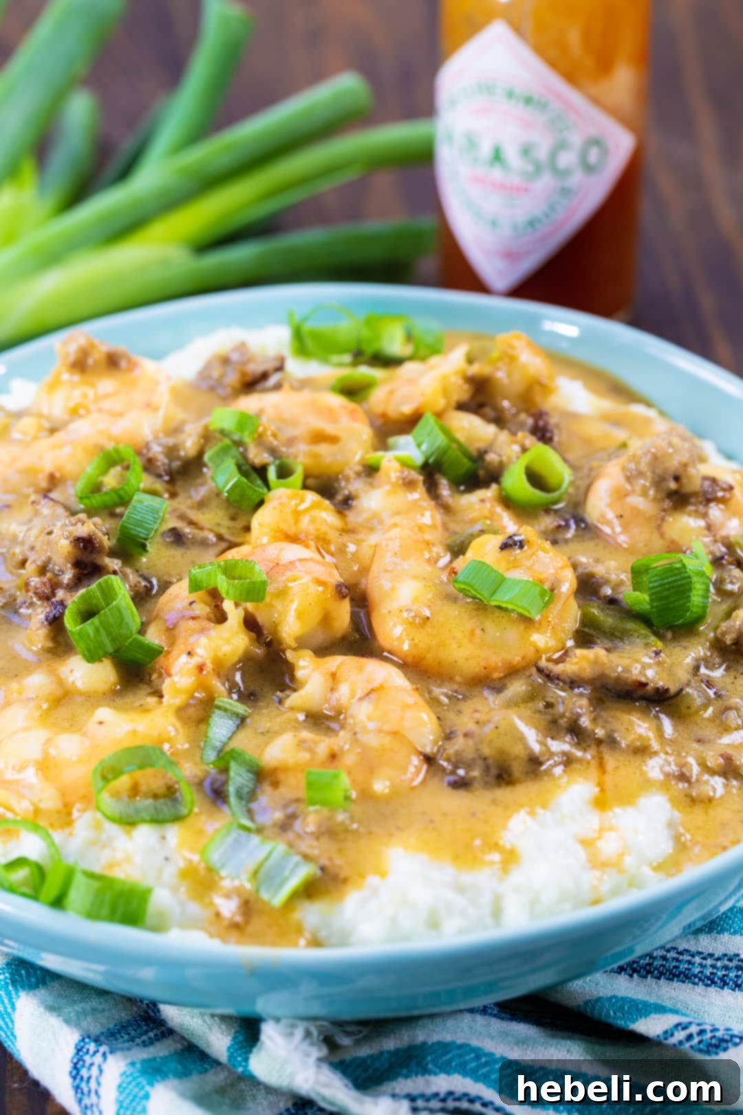 A close-up view of Sausage Gravy Shrimp and Grits, showcasing the rich, thick gravy clinging to the shrimp and covering the creamy grits, garnished with fresh green onions.