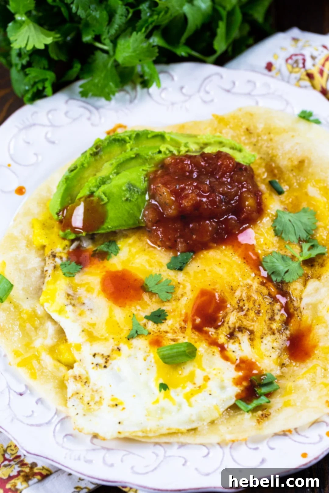 A close-up of a beautifully cooked Tortilla Egg, garnished with fresh salsa, sliced avocado, and a sprinkle of cilantro, presented on a white plate.