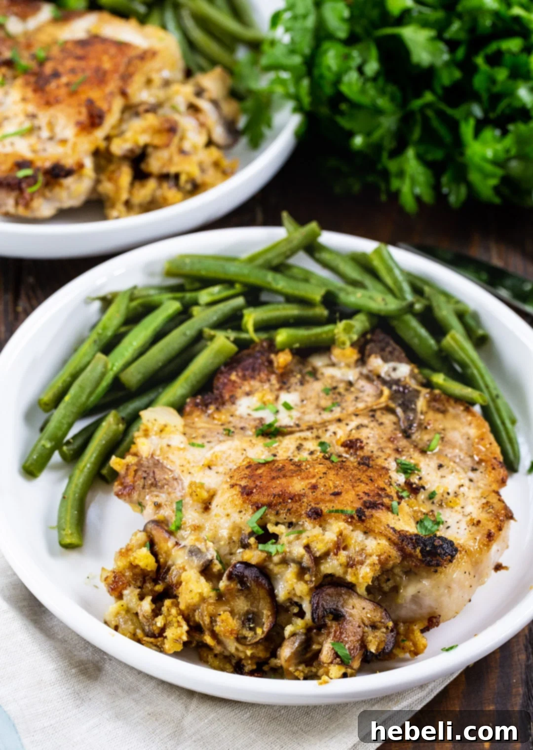 Two Cornbread Stuffed Pork Chops on a plate with green beans, showcasing the delicious golden-brown crust.