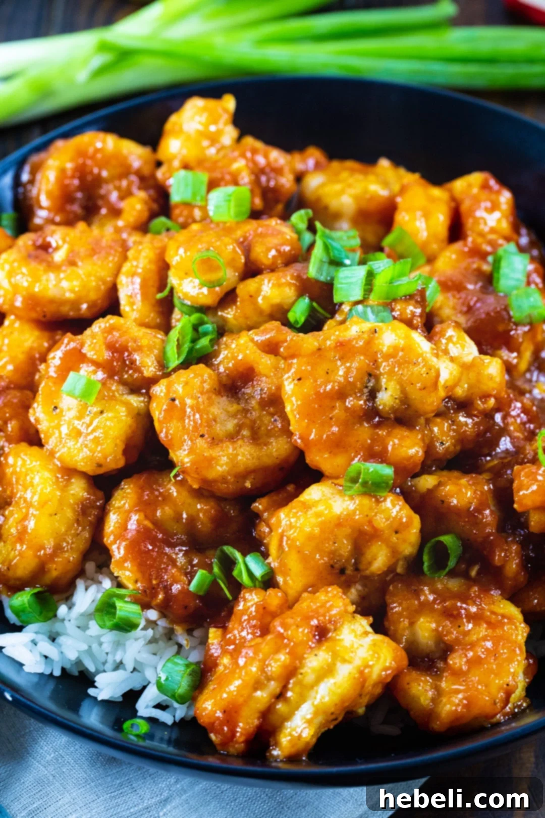 Close-up of Gochujang Shrimp served elegantly over white rice in a black bowl.