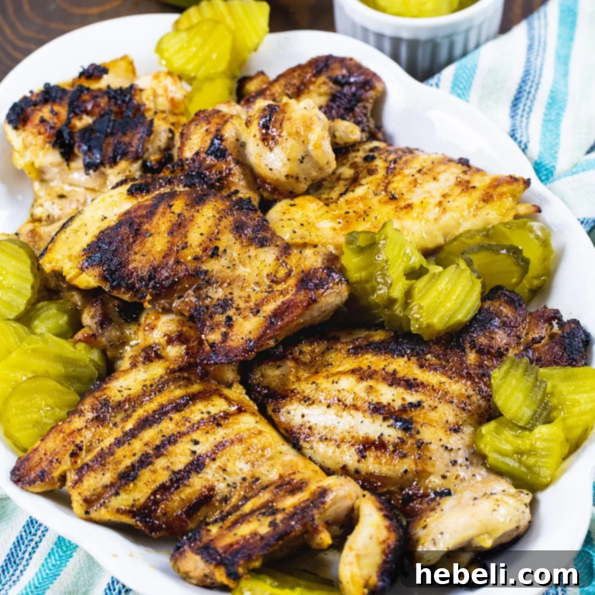 Golden-brown Pickle-Brined Grilled Chicken thighs on a serving platter, garnished with fresh dill pickle chips, highlighting its juicy interior.