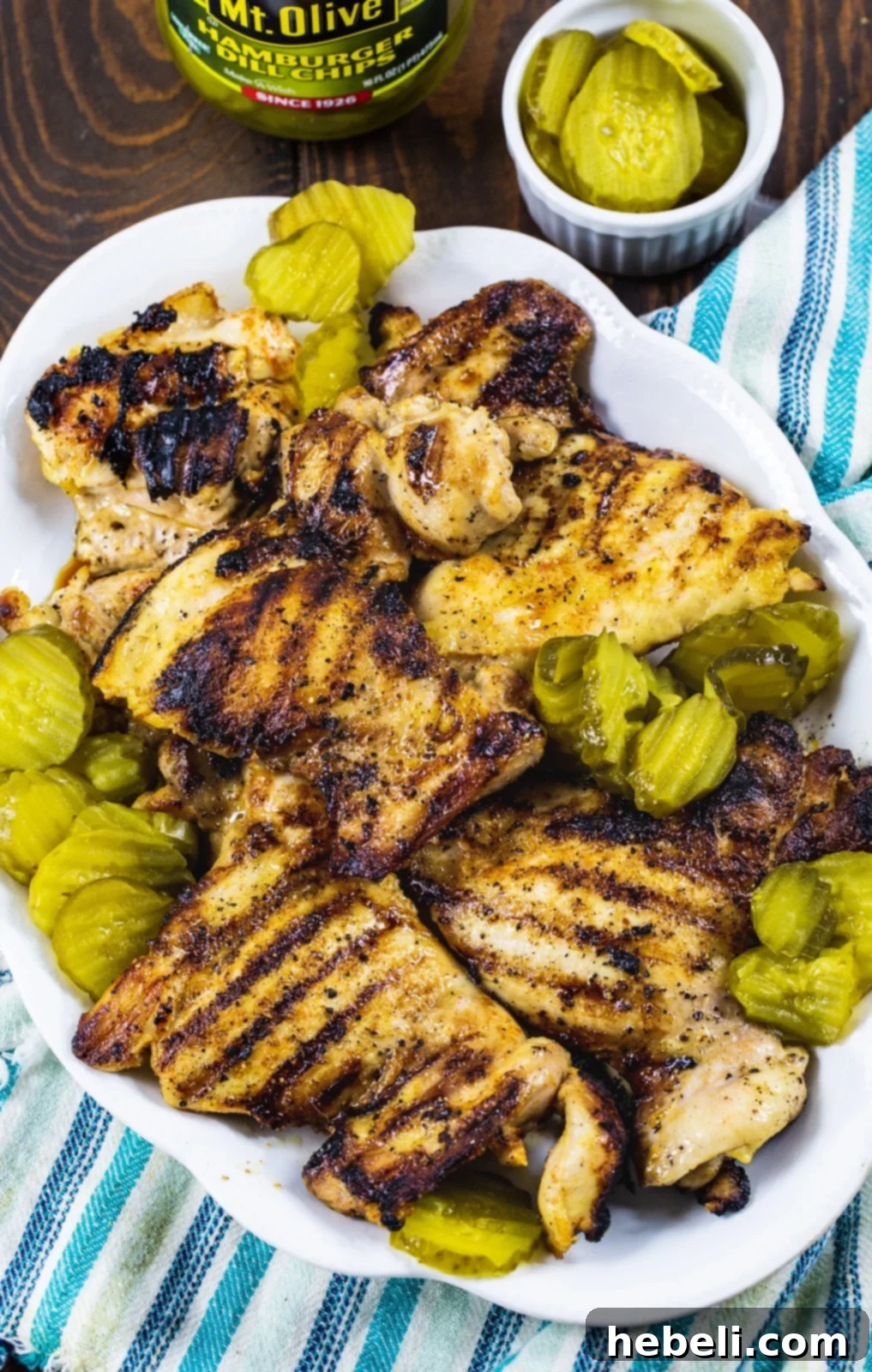 Succulent grilled chicken on a serving platter, perfectly cooked with a golden crust, surrounded by fresh pickle slices, ready to be enjoyed.