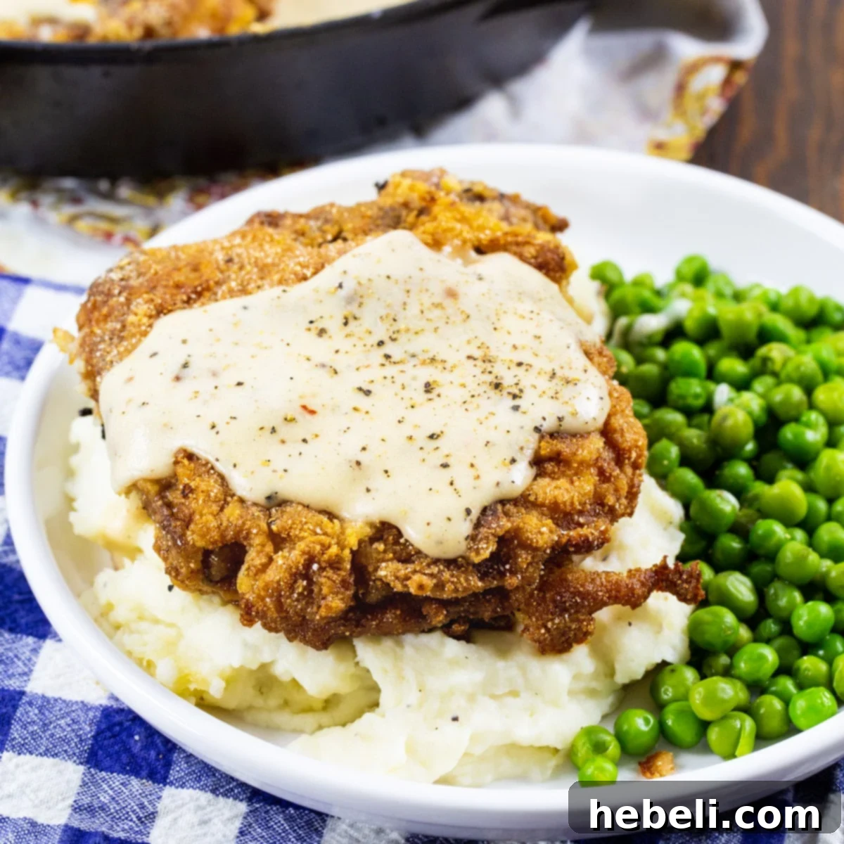 Crispy Southern Fried Pork Chop on a plate with vibrant green peas and fluffy mashed potatoes, drizzled with creamy white gravy.