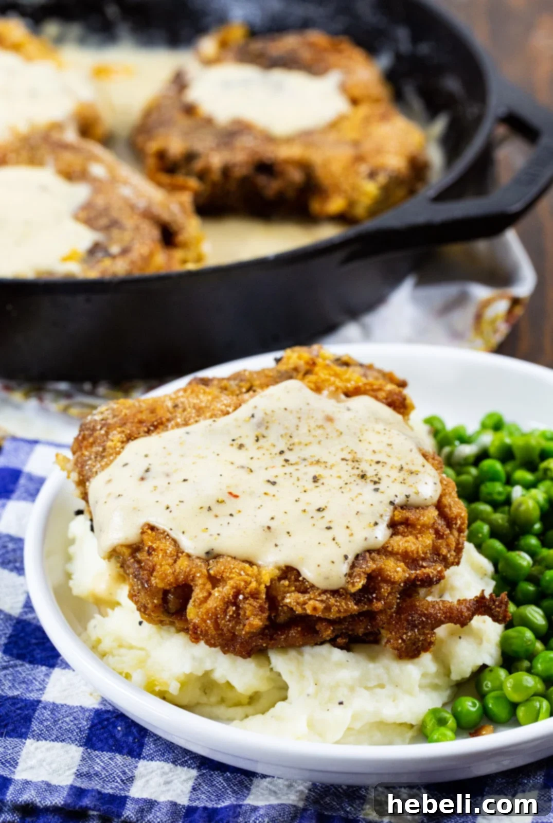 Southern Fried Pork Chop with White Gravy on a plate, served with mashed potatoes and green peas, ready to be enjoyed.