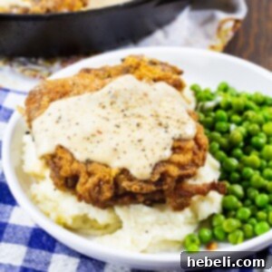 A finished Southern Fried Pork Chop with White Gravy in the corner of a plate