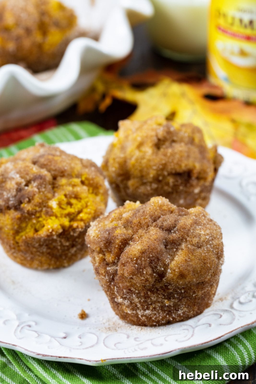 Three perfectly baked Pumpkin Doughnut Muffins arranged on a white plate, showcasing their inviting golden color and cinnamon sugar coating.