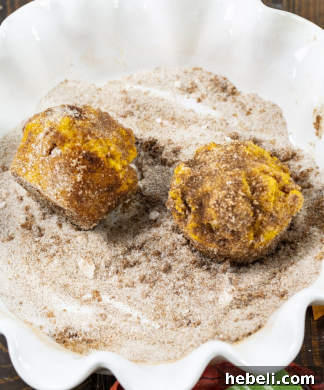 A close-up shot of a baked muffin being rolled in a bowl of cinnamon sugar, showing the coating process.